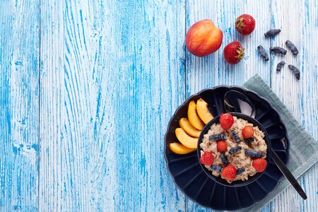 Oatmeal porridge with fresh berries and fruit in dark blue bowl on blue wooden background. Top view with copy space. Concept of healthy lifestyle, healthy food, dieting, vegetarian foodの写真素材