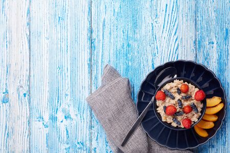 Oatmeal porridge with fresh berries and fruit in dark blue bowl on blue wooden background. Top view with copy space. Concept of healthy lifestyle, healthy food, dieting, vegetarian foodの写真素材