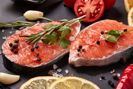 Fresh raw steak of salmon with spices and vegetables lying on stone cutting board on a black background. Seafood menuの写真素材