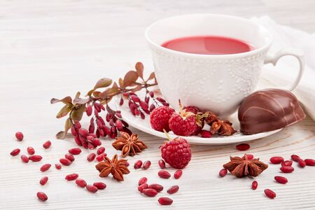 Healthy fruit tea with anise, barberries and raspberries in white porcelain cup and branch of...