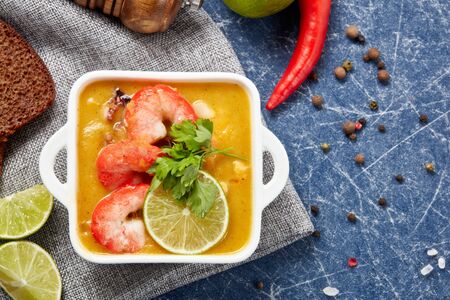 Delicious  fish cream soup with shrimps in white bowl served with spices, lime and pieces of bread on dark blue marble background. Top view. Healthy food. Seafood menuの写真素材