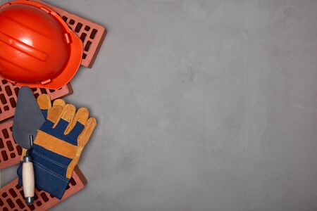 Construction concept. Stack of new bricks with masonry trowel, construction orange hard hat and protective  gloves on gray concrete background. Top view with copy space.の写真素材