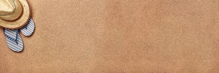 Male beach accessories: flip flops and straw hat on sand background.  Top view with copy space....