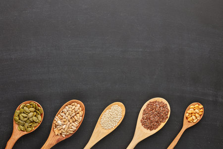 Various varieties of nuts and seeds lying in wooden spoones on black slate background. Top view with copy space. Healthy food. Vegetarian nutritionの写真素材