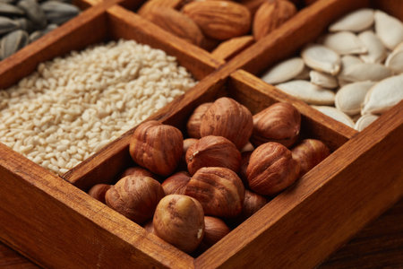 Various varieties of nuts and dried seeds lying in wooden box on brown wooden background. Top view. Healthy food. Vegetarian nutrition. Selective focus on hazelnutsの写真素材