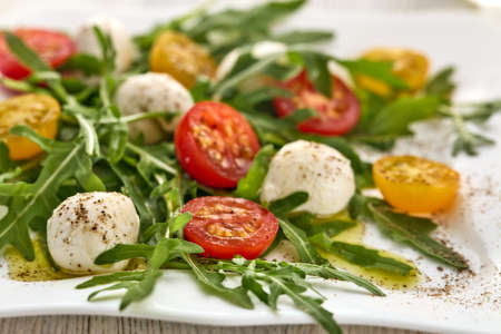 White plate with dietary salad from mozzarella cheese, cherry tomatoes and leaves of arugula, table setting.の写真素材