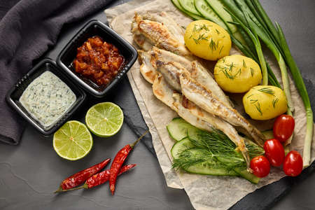 Fried smelts serving with vegetables,  lime and sauces, glass mug with beer on grey slate background. Top view.の写真素材
