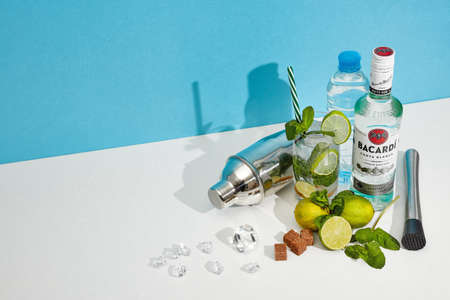 St.Petersburg, Russia - February 2021 - Mojito cocktail. Bottle of Bacardi white rum, glass with cocktail, bar accessories on double white blue background with shadow. Copy spaceのeditorial素材