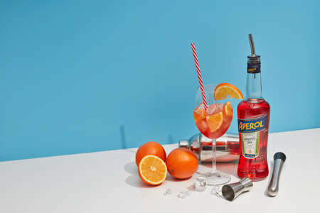 St.Petersburg, Russia - February 2021 - Cocktail Aperol spritz. Bottle of Aperol aperitivo, oranges and glass with cocktail standing on white table on blue background.のeditorial素材