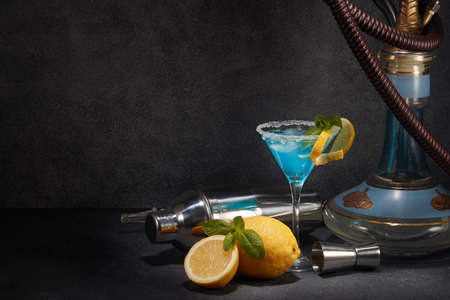 Hookah (shisha) and glass of Blue curacao cocktail with lemon and mint on dark gray background with copy space. Hookah bar. Weekend or holiday partyの写真素材