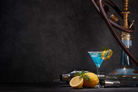 Hookah (shisha) and glass of Blue curacao cocktail with lemon and mint on dark gray background with...