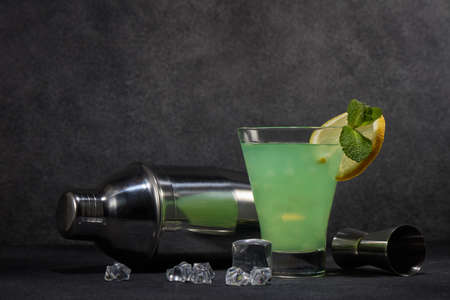 Glass of cold cocktail with fresh mint and lemon, bar tools on dark grey background. Cocktail bar. Party.の写真素材