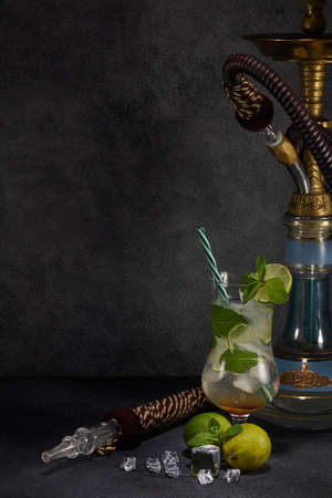 Hookah (shisha) and glass of Mojito cocktail with lime and ice on dark grey background with copy...