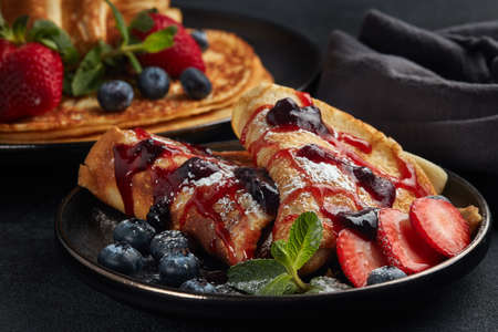 Pancakes with berries  and sweet sauce on black background.  Maslenitsa. Shrovetide. Shrove Tuesday....