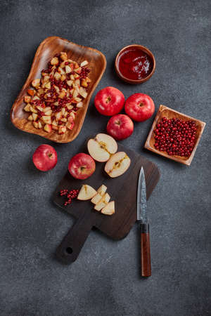 Still life with fresh lingonberries, red appples with knife on black cutting board and  homemade jam on wooden bowl on dark background. Top view. Autumn harvest, Home canning.の写真素材