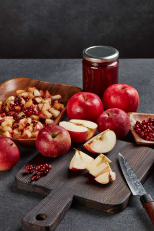 Still life with fresh lingonberries, red appples with knife on black cutting board and jar of homemade jam on dark background. Autumn harvest, Home canning.の写真素材