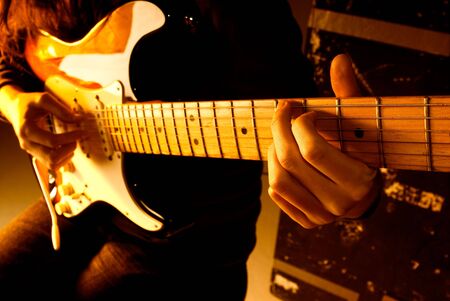 Musician playing guitar at studio with shallow depth of field and orange lighting. 