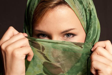 Young arab woman with veil showing her eyes on dark gray backgroundの写真素材