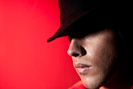 Handsome man portrait with hat dark eyes mistery and beauty concept on red backgroundの写真素材