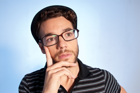 Young man modern nerd thinking with hat and glasses wide angle close up portrait on blue backgroundのeditorial素材