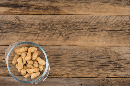 Peanuts in a glass bowl on the old wooden table. Top view.