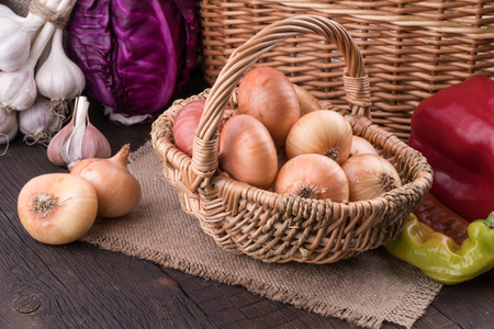 Onions in a wicker basket on old wooden table. Selective focus.の写真素材