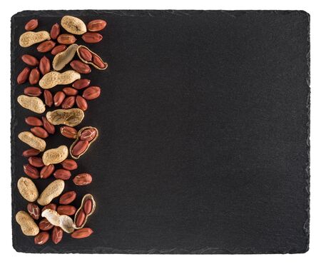 Peanuts on black slate board. Isolated on white background. Top view.