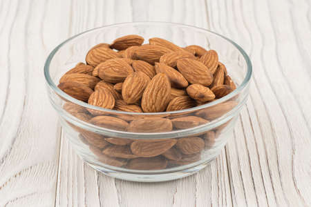 Almonds in a glass bowl on white old wooden table. Selective focus.