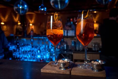 two orange alcoholic coctail with ice on a wooden stand
