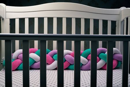 Fence in the shadow of empty children 's wooden white crib with multicolored braid, fences soft for rib. White in a dot sheet. Cozy bed for the baby. subject photoの写真素材