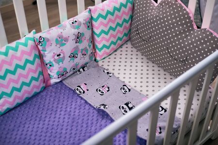 Multicolored pillows with different patterns lie in a children 's white tree crib on a white sheet...