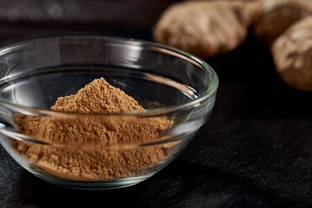 Ground ginger in a plate on a black background. In the background, the root of ginger. side view. sharp powder. macro photo. Against viruses and diseases. studio photoの写真素材