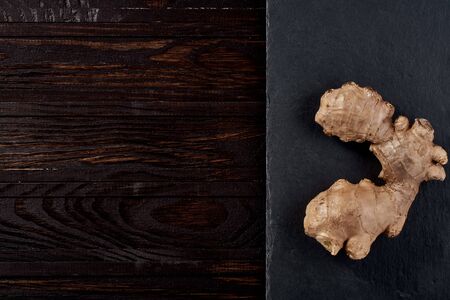 The root of ginger lies on a stone rectangular plate on a tree brown table. top view. immunity against viruses. macro photoの写真素材