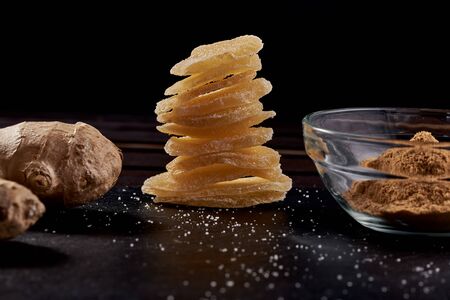 Slices of ginger dried fruit near which lies ground ginger in a plate and ginger root on a stone...