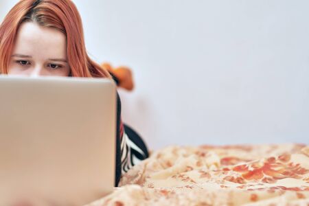 A girl with pink hair and no makeup lies on the couch and looks closely into the grey laptop. it is visible only eyes. Entertained, worked and studied at home. covid-19. stay at home. work homeの写真素材