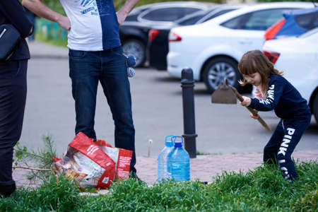 Kyiv, Ukraine, 02.05.2020: A girl with her parents sits a tree on the lawn. The girl processes the ground to plant the tree. parents observe.のeditorial素材