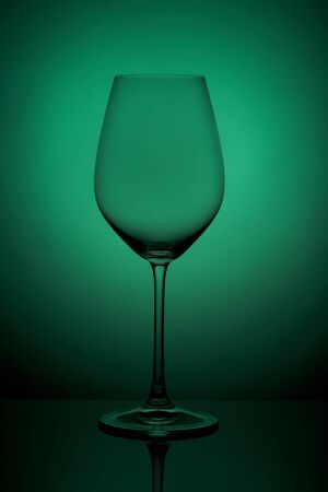 The crystal glass stands on the reflecting surface on a green background. studio photo. product. Beautiful shadow from wine glass. macro photo.の写真素材