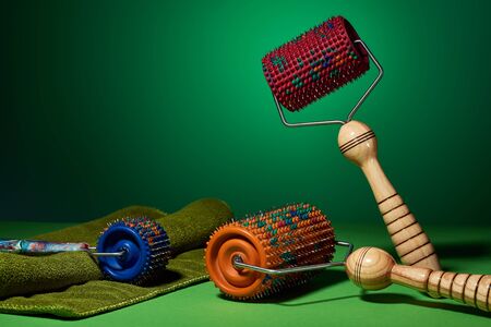 Three masseurs with orange, blue and red drums, metallic needles on a green background lie near the...