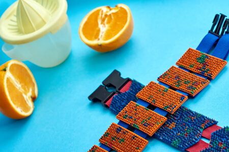 Zone massager. A blue belt with orange boxes from rubber and metal spikes lay on a blue background next to an orange and juice extractor. Advertising, thematic and subject shooting. For relaxation and healthの写真素材