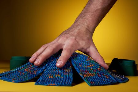 A blue massage mat shaped like chamomile lies on a yellow background with hand. Advertising,...