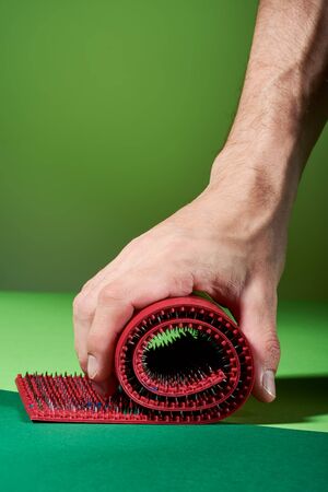 The hand holds a twisted massager in the form of a red carpet with metal spikes lying on green backgrounds, a side view. Advertising, thematic and subject shooting. For relaxation and healthの写真素材