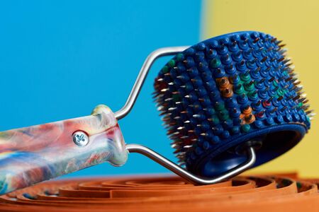 A blue massager with rubber and spikes, metal needles, lie on a green ribbon on a yellow-blue background. Advertising, For relaxation and health.の写真素材