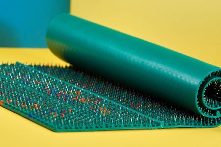 A wide massager in the form of a green carpet with spikes, metal needles, lies on a yellow-blue background. Thematic and thematic shooting. For relaxation and healthの写真素材