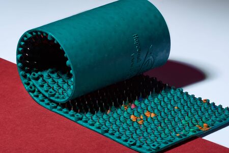 Massager in the form of green twisted carpet with metal spikes, needles, lies on red and white backgrounds, diagonal. Abstraction. Thematic and thematic shooting. For health of a relaxationの写真素材