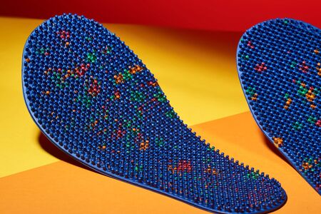 Blue massage insole for feet, with metal needles, spikes, on a yellow-orange background. For relaxation and health. Advertising, thematic and subject shootingの写真素材