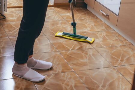 A woman washes the floor of tiles in the kitchen with a mop. Cleaning of the apartment. yellow rag. cleaning house cleaning. we kill microbes.の写真素材