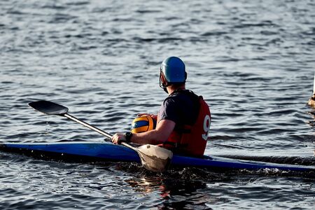 A guy wearing a canoe polo helmet rowing on a paddle and sailing on water with a ball in his hands. canupolo. puts on rescue yellow. rear view.の写真素材