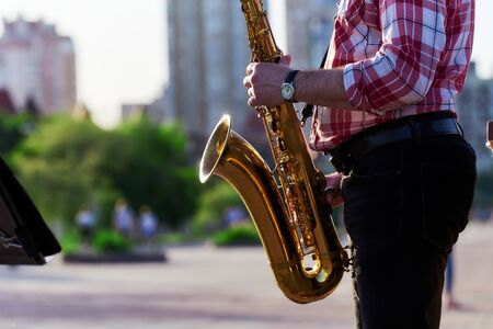 saxophonist plays a golden saxophone on the street with passers-by in sight. spring. musical reed wind instrument. tongue wooden brass musical instrument.の写真素材
