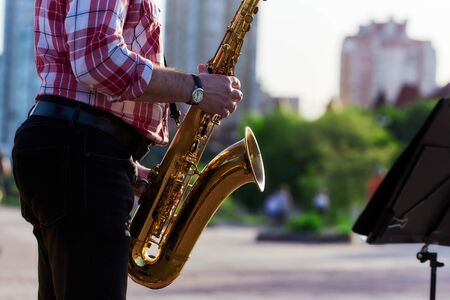 saxophonist plays a golden saxophone on the street with passers-by in sight. spring. musical reed wind instrument. tongue wooden brass instrument.の写真素材