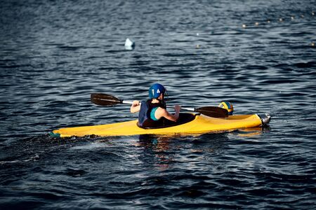 A guy wearing a helmet on a canoe polo rowing a paddle and sailing on water. canupolo. puts on a rescue yellow. rear view. water splashesの写真素材